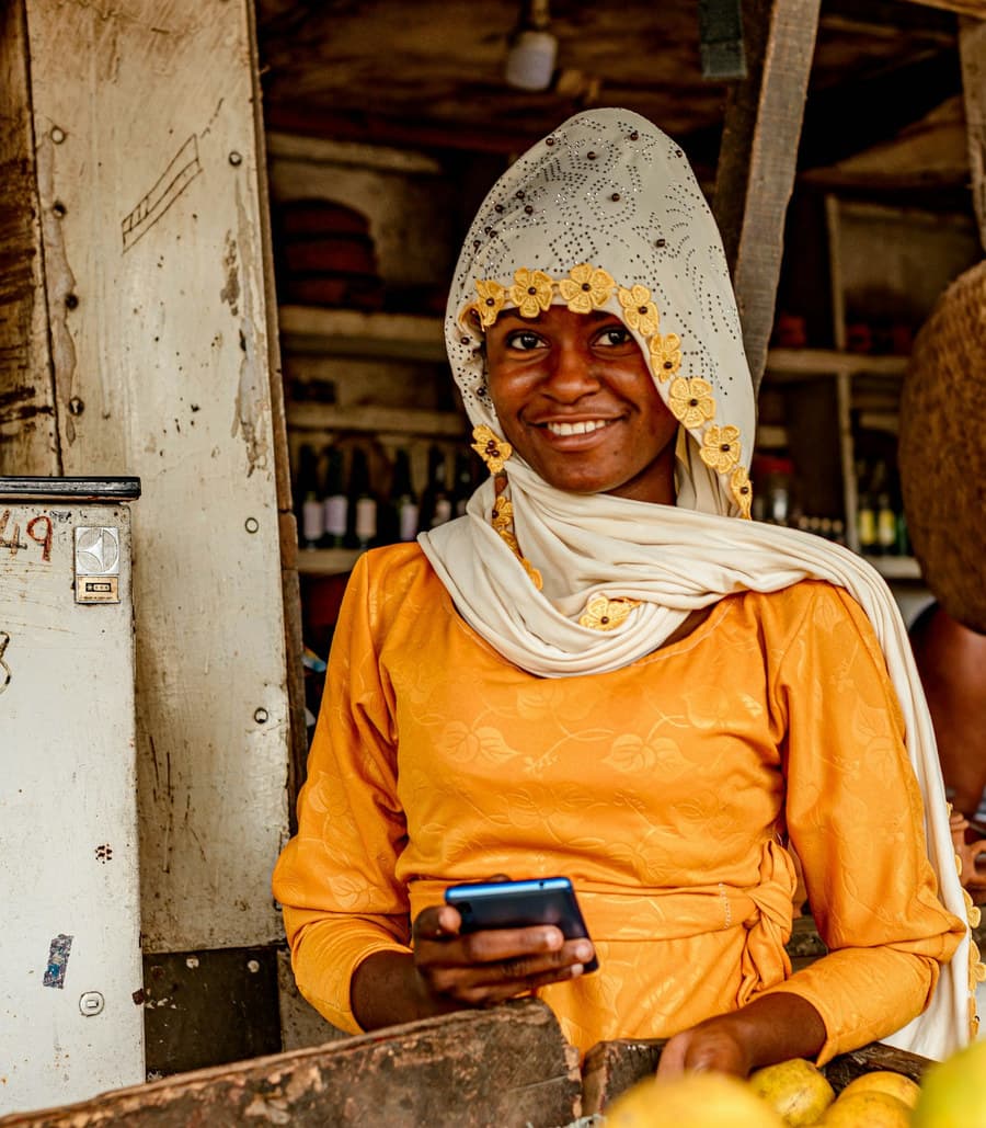 A trader smiling while using a mobile phone at her stall
